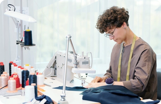 pretty young seamstress sitting by sewing machine and processing blue textile e1627088678669